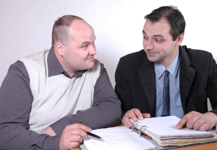 two men looking at each other pointing to open folder