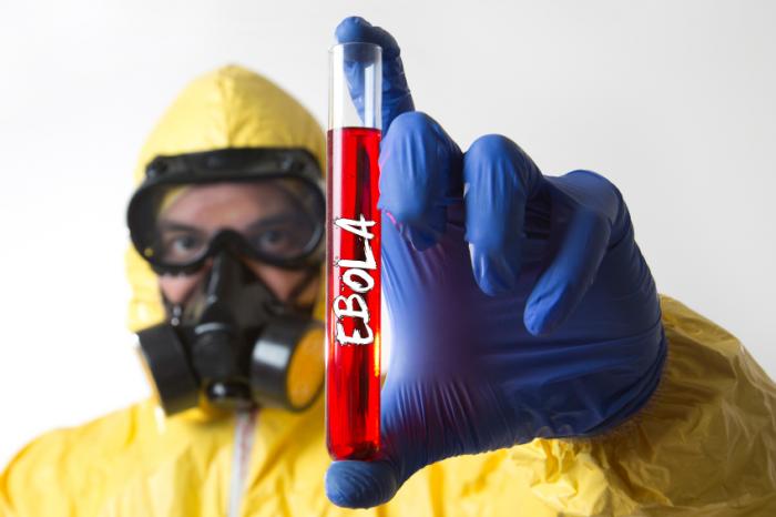 Person in hazardous materials outfit holding Ebola test tube.