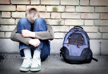 unhappy teen hugging his knees with backpack nearby