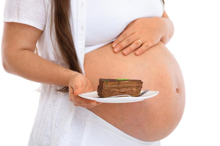 [A pregnant woman holding a slice of cake]