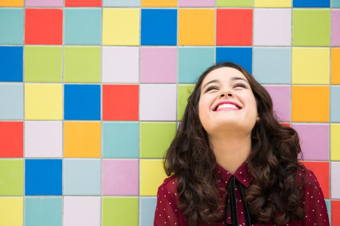 Happy woman standing next to colorful wall]