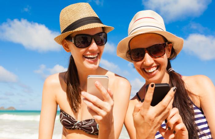 [Two women staring at cell phones on a beach]