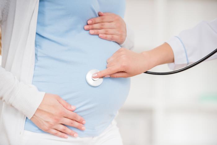 [A doctor placing a stethoscope on a pregnant woman's belly]