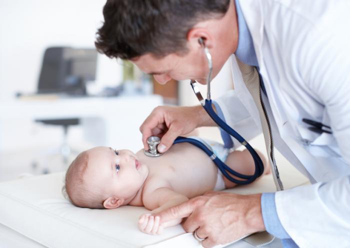A doctor uses his stethoscope to examine a baby on a table
