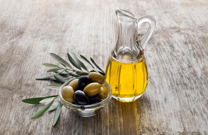 A jug of olive oil with a dish of olives.