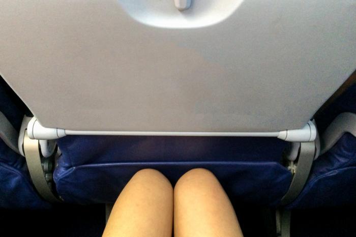 A ladys knees touching the seat in front on an airplane