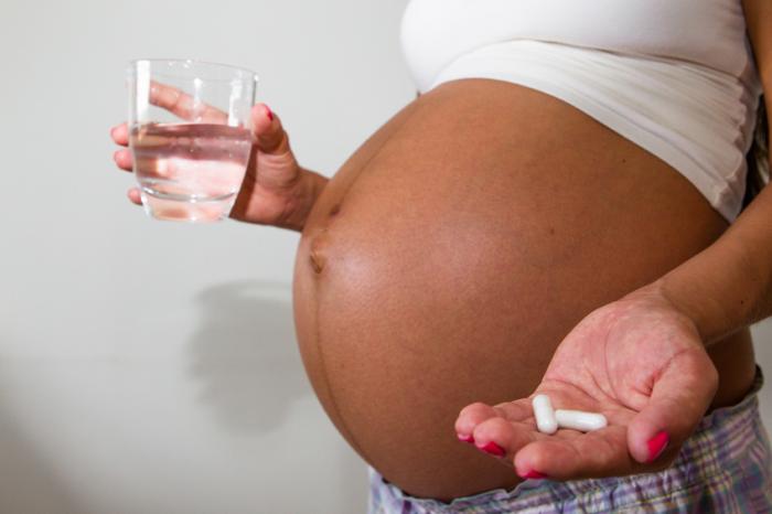 [A pregnant woman holding pills and a glass of water]