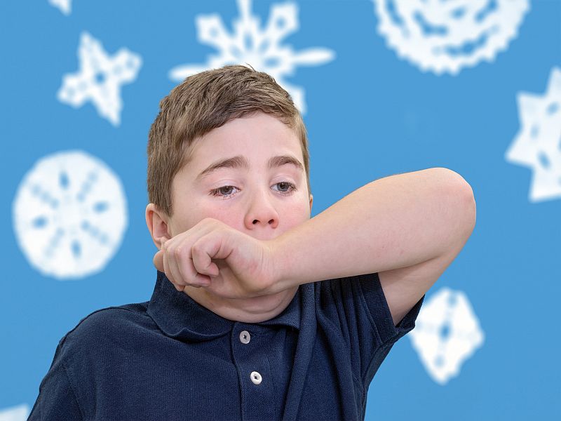 Ill child covering his mouth with his arm to contain sneeze