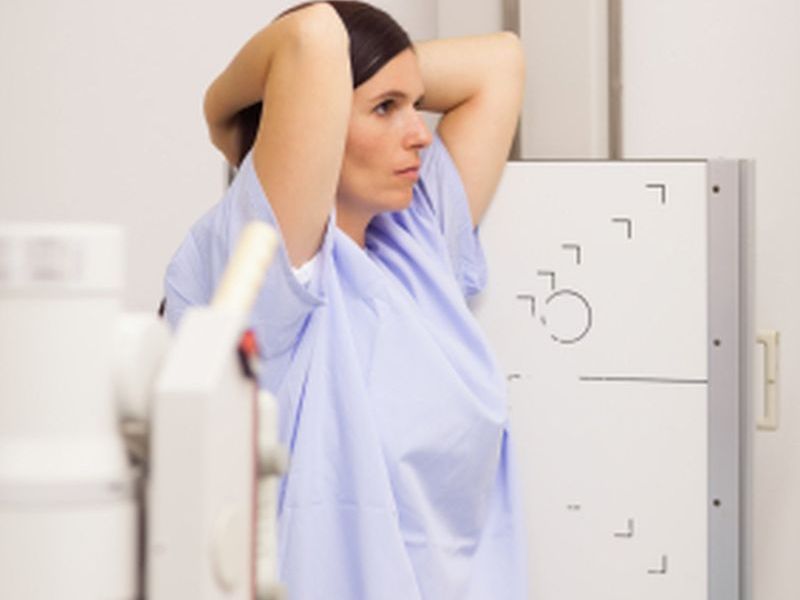 Woman placing her arms on her head while standing in front of a machine in an examination room